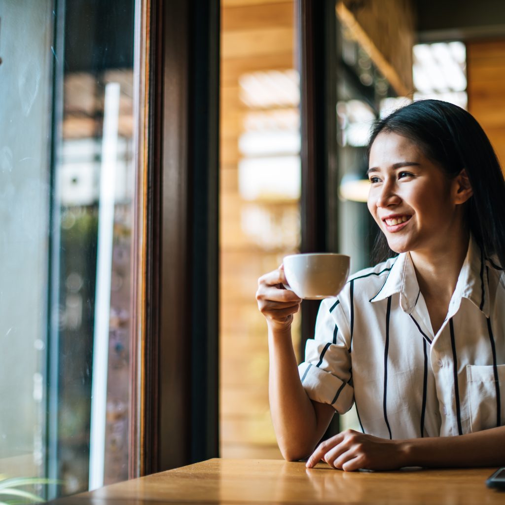 Seorang perempuan duduk di kafe sambil memegang secangkir kopi herbal.